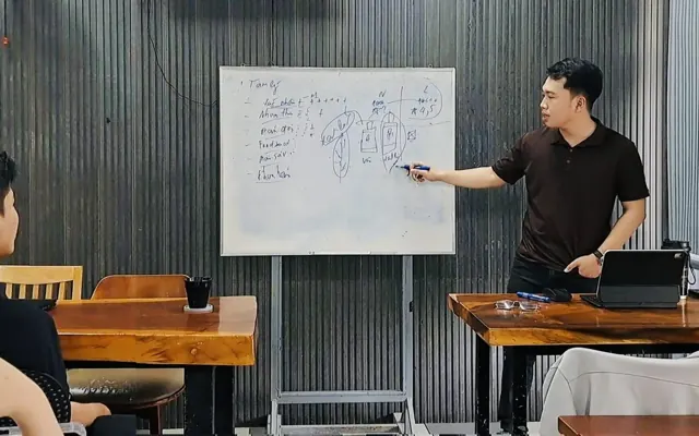 Quốc Hiệp đứng trước bảng trắng trình bày sơ đồ trong một buổi đào tạo