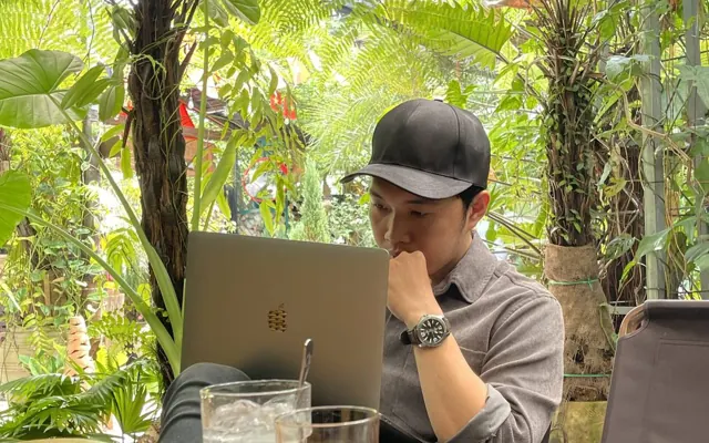 Quốc Hiệp ngồi làm việc với laptop trong một quán cà phê sân vườn